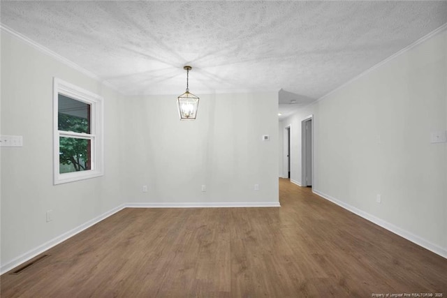 empty room featuring wood finished floors, a textured ceiling, visible vents, baseboards, and ornamental molding