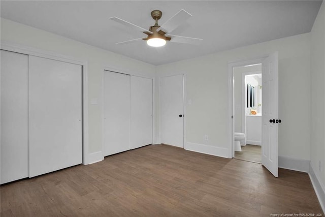 unfurnished bedroom with baseboards, two closets, a ceiling fan, and wood finished floors