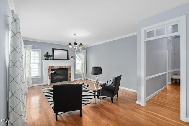 living area featuring wood finished floors, baseboards, a chandelier, a brick fireplace, and ornamental molding