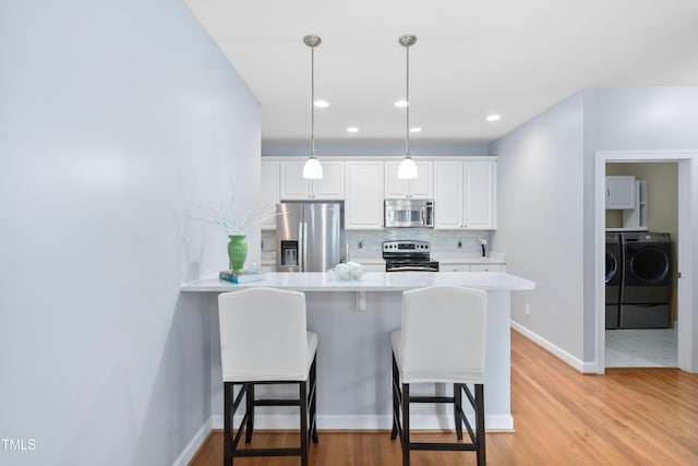 kitchen featuring stainless steel appliances, independent washer and dryer, a kitchen bar, white cabinets, and recessed lighting