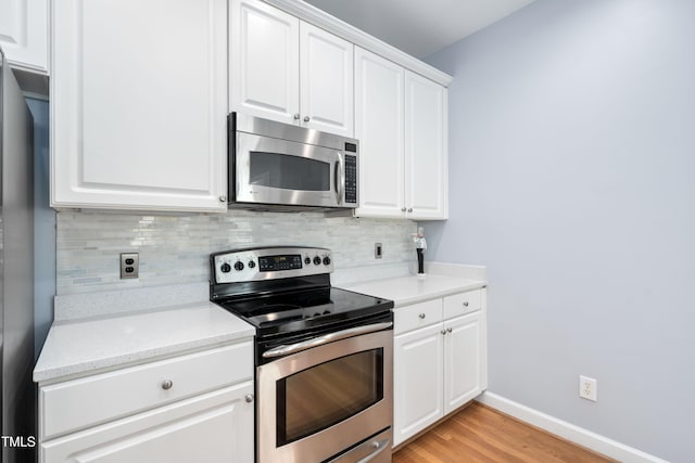 kitchen with appliances with stainless steel finishes, tasteful backsplash, baseboards, light wood finished floors, and white cabinetry