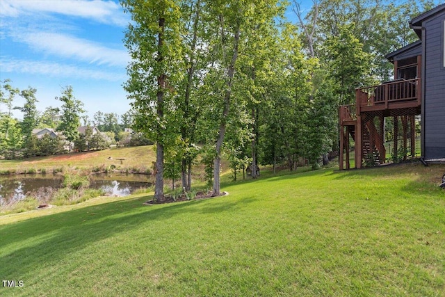 view of grassy yard featuring stairs and a deck with water view