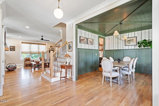 dining room featuring a ceiling fan, wood finished floors, a decorative wall, stairway, and vaulted ceiling