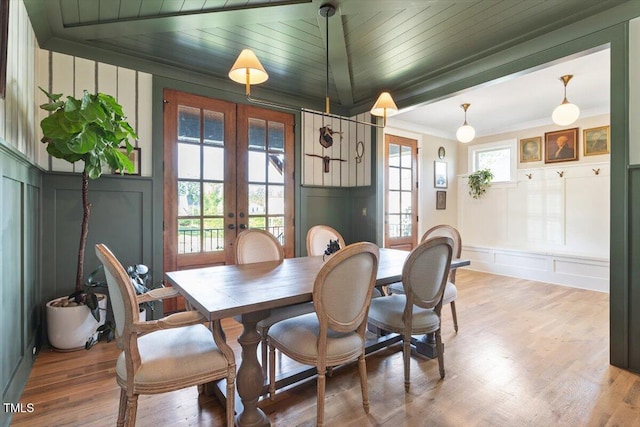 dining space with a decorative wall, french doors, light wood-style floors, ornamental molding, and wooden ceiling
