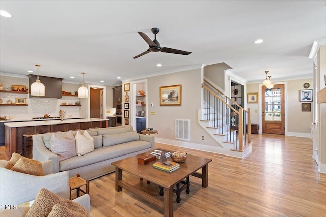 living room featuring stairway, baseboards, ornamental molding, ceiling fan, and light wood finished floors