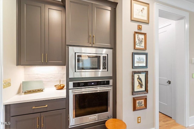 kitchen featuring stainless steel appliances, gray cabinetry, tasteful backsplash, light countertops, and light wood-style floors