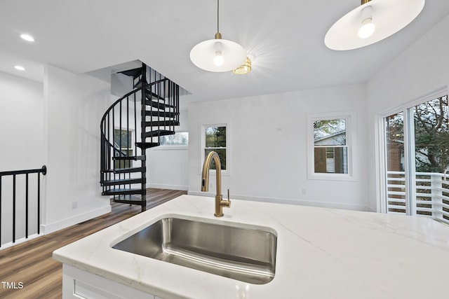 kitchen with a sink, wood finished floors, decorative light fixtures, light stone counters, and baseboards