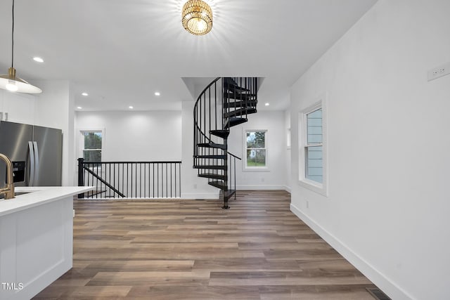 unfurnished living room with healthy amount of natural light, wood finished floors, recessed lighting, baseboards, and a sink
