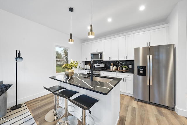 kitchen with appliances with stainless steel finishes, decorative backsplash, white cabinets, a sink, and light wood-type flooring