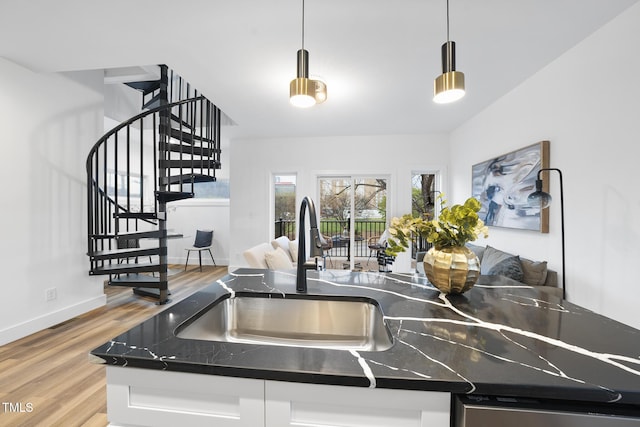 kitchen featuring a sink, light wood-type flooring, open floor plan, dark countertops, and pendant lighting
