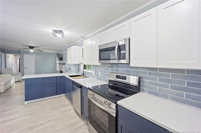 kitchen with a sink, open floor plan, a peninsula, tasteful backsplash, and appliances with stainless steel finishes