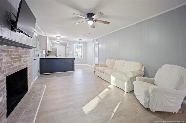 living room featuring a fireplace, crown molding, light wood-style flooring, a ceiling fan, and baseboards