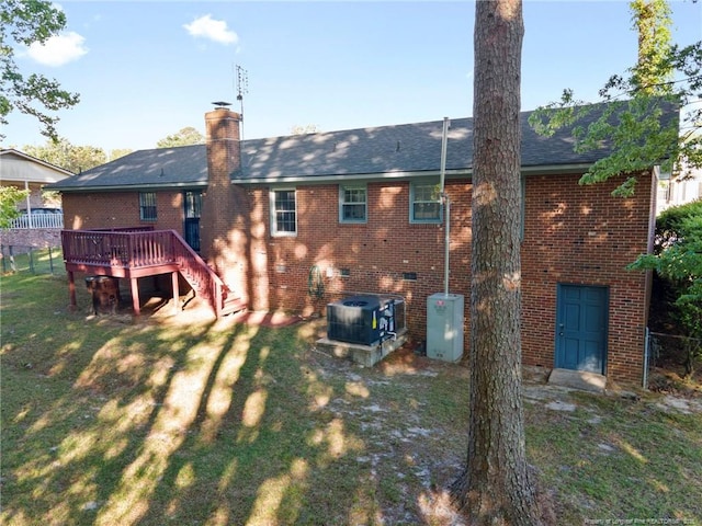 rear view of house featuring cooling unit, a chimney, a wooden deck, a lawn, and brick siding