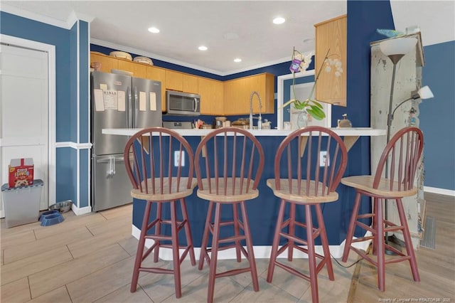 kitchen featuring baseboards, ornamental molding, a peninsula, stainless steel appliances, and light wood-type flooring