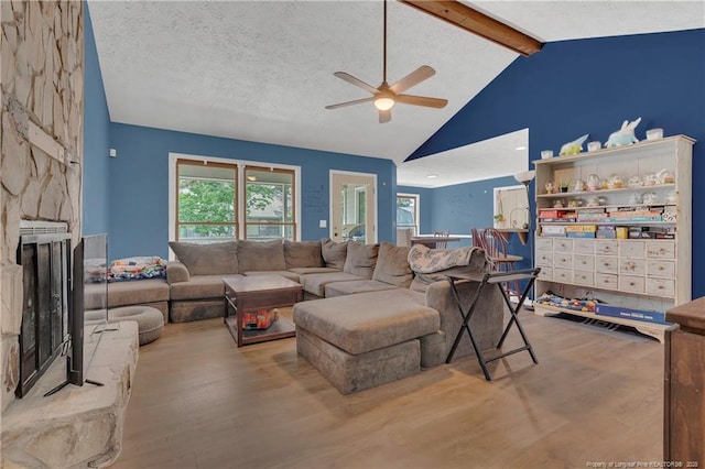 living area featuring wood finished floors, a ceiling fan, high vaulted ceiling, a fireplace, and beamed ceiling