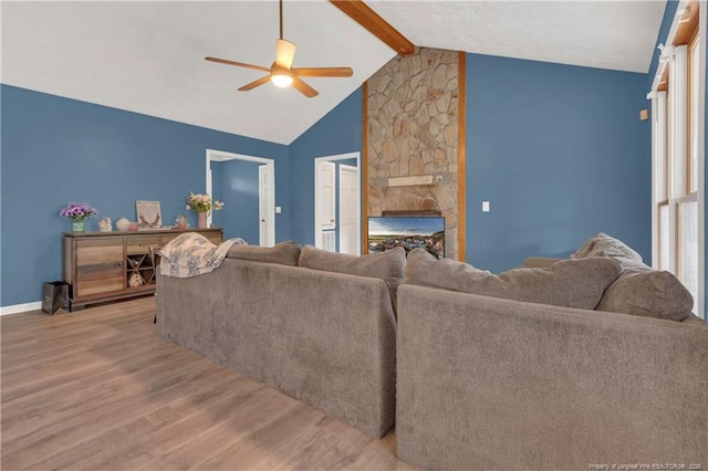 living area featuring a fireplace, ceiling fan, light wood finished floors, baseboards, and vaulted ceiling with beams