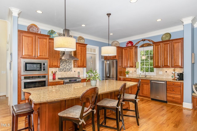 kitchen with appliances with stainless steel finishes, a sink, light wood finished floors, a kitchen island, and ornamental molding