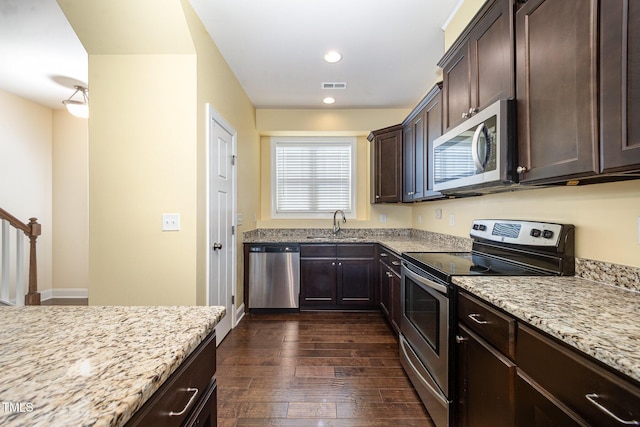 kitchen with appliances with stainless steel finishes, dark brown cabinetry, dark wood-style floors, light stone countertops, and recessed lighting