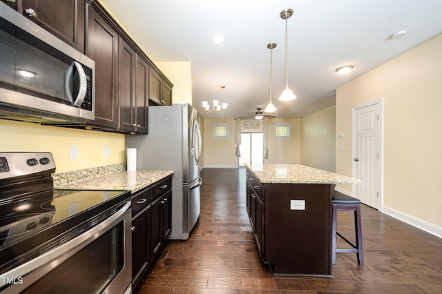 kitchen with appliances with stainless steel finishes, a kitchen bar, a center island, dark wood-type flooring, and dark brown cabinetry