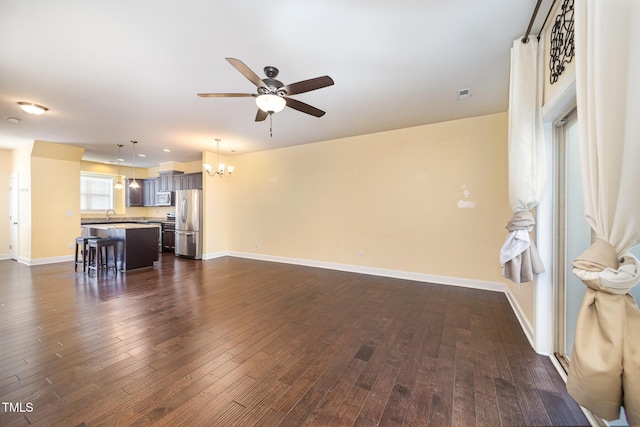 living area with a ceiling fan, a chandelier, dark wood-style floors, and baseboards