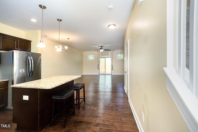 kitchen featuring dark brown cabinets, dark wood-style flooring, a kitchen island, a ceiling fan, and a kitchen bar