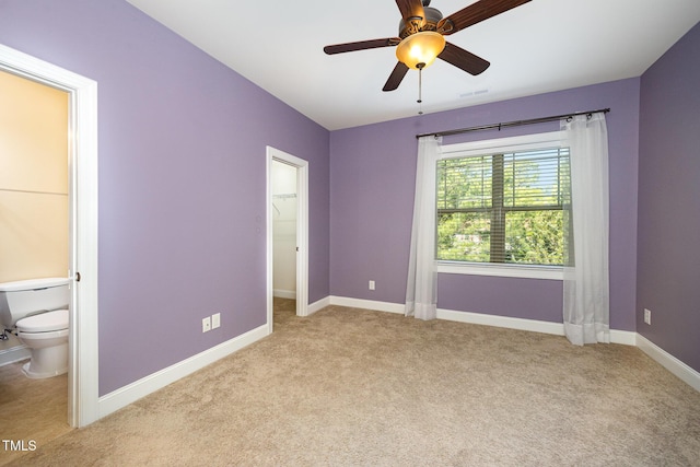 unfurnished bedroom featuring a spacious closet, light colored carpet, baseboards, ensuite bathroom, and ceiling fan