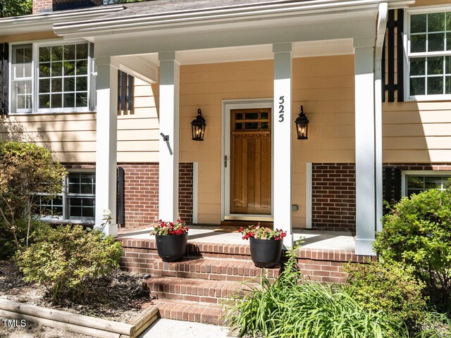 property entrance with covered porch, brick siding, and a chimney