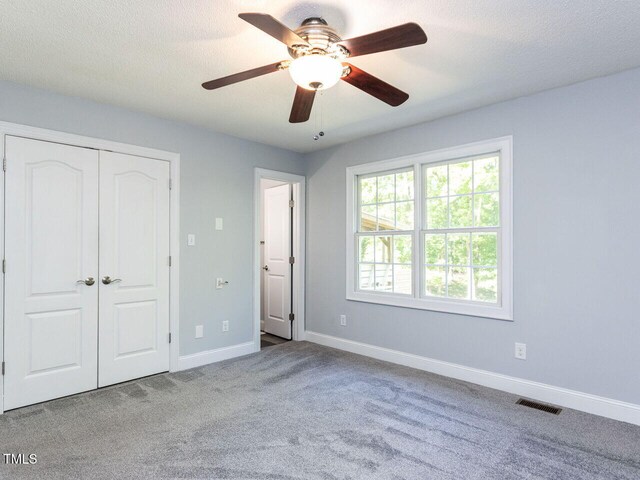 unfurnished bedroom featuring carpet, baseboards, a closet, ceiling fan, and a textured ceiling
