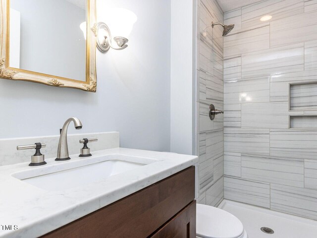 full bathroom with tiled shower, toilet, and vanity