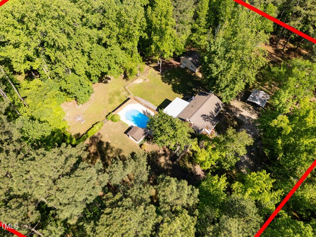 drone / aerial view of a pool area and a heavily wooded area