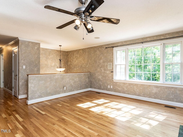 spare room featuring wood finished floors, crown molding, a ceiling fan, and baseboards
