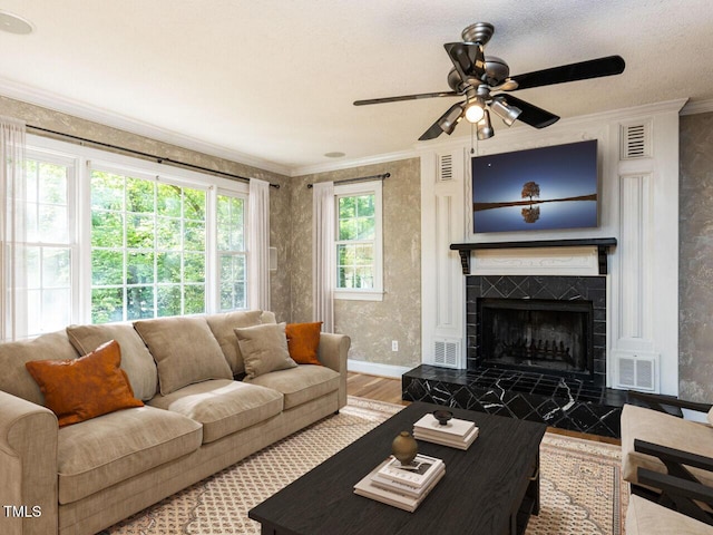 living area with wood finished floors, ornamental molding, a ceiling fan, a fireplace, and baseboards