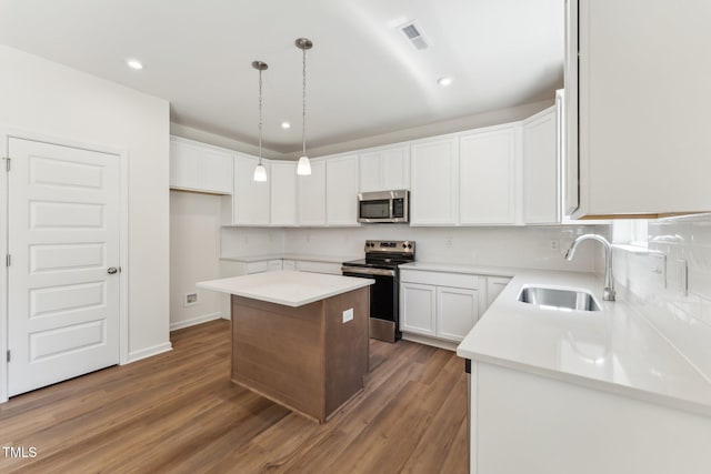 kitchen featuring appliances with stainless steel finishes, a sink, a kitchen island, decorative backsplash, and wood finished floors