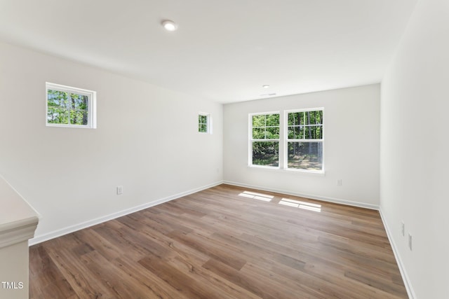 empty room featuring plenty of natural light, baseboards, wood finished floors, and recessed lighting