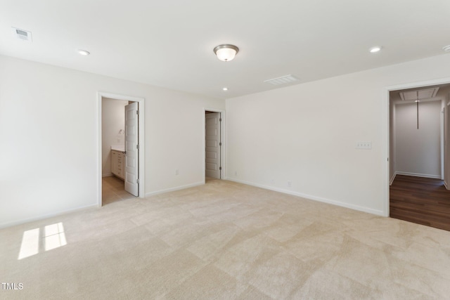 unfurnished bedroom with attic access, light carpet, baseboards, recessed lighting, and ensuite bath