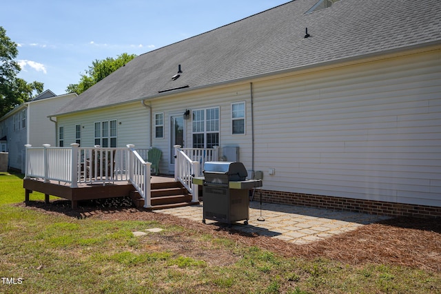 back of property with a deck, roof with shingles, a lawn, and a patio area