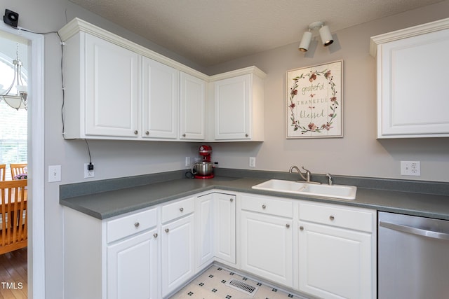 kitchen with dishwasher, a sink, dark countertops, white cabinets, and a textured ceiling