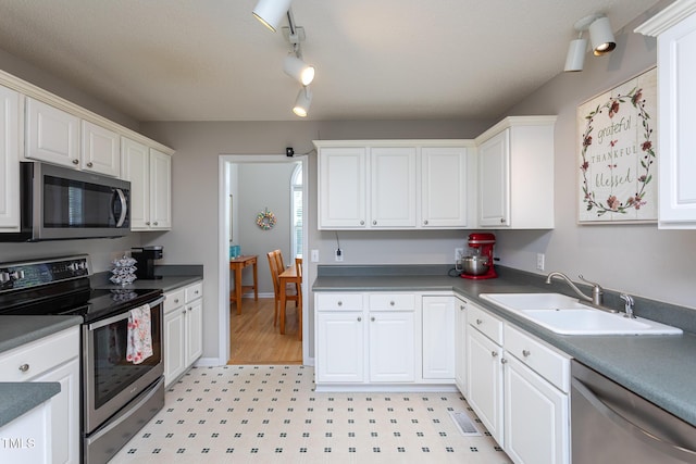 kitchen featuring stainless steel appliances, a sink, light flooring, and white cabinetry