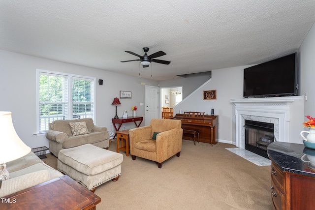 living room featuring a ceiling fan, a high end fireplace, light carpet, and a textured ceiling