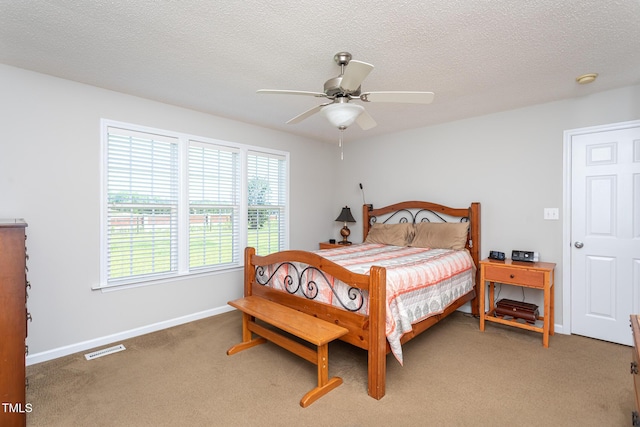 bedroom with multiple windows, light colored carpet, baseboards, a ceiling fan, and a textured ceiling