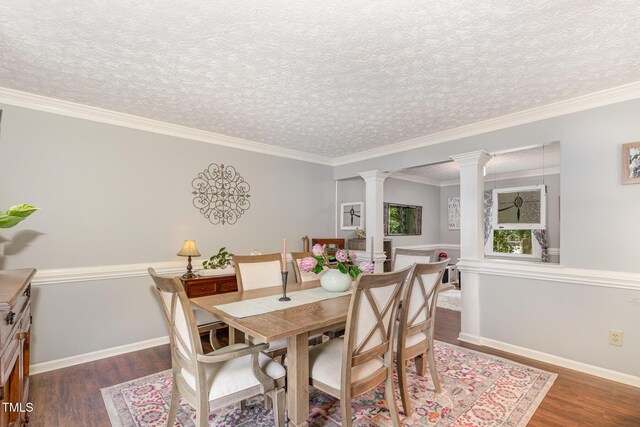 dining room featuring ornate columns, wood finished floors, baseboards, a textured ceiling, and crown molding