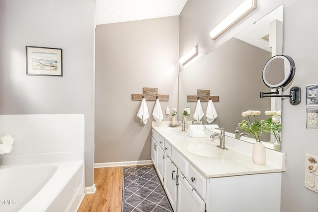 bathroom featuring a bath, wood finished floors, double vanity, and baseboards