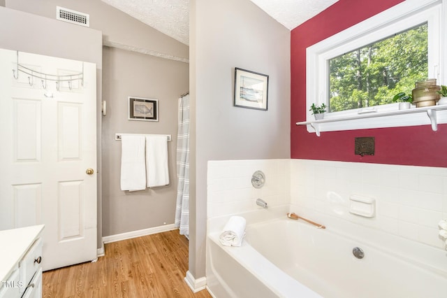 bathroom with wood finished floors, a garden tub, baseboards, vanity, and a textured ceiling
