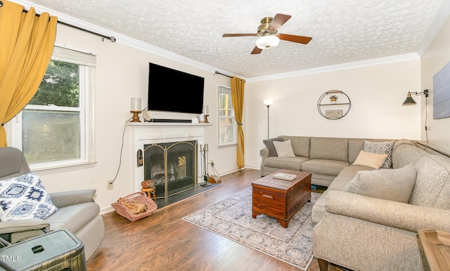 living area with wood finished floors, a fireplace with raised hearth, a textured ceiling, a ceiling fan, and baseboards