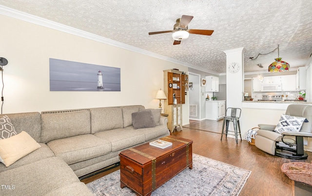 living area featuring dark wood-style flooring, ceiling fan, ornamental molding, and a textured ceiling