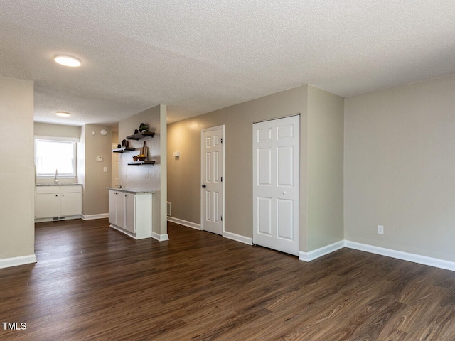 unfurnished living room with dark wood-style floors, a textured ceiling, a sink, and baseboards