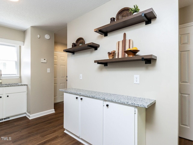 kitchen featuring open shelves, dark wood-type flooring, white cabinetry, baseboards, and light stone counters