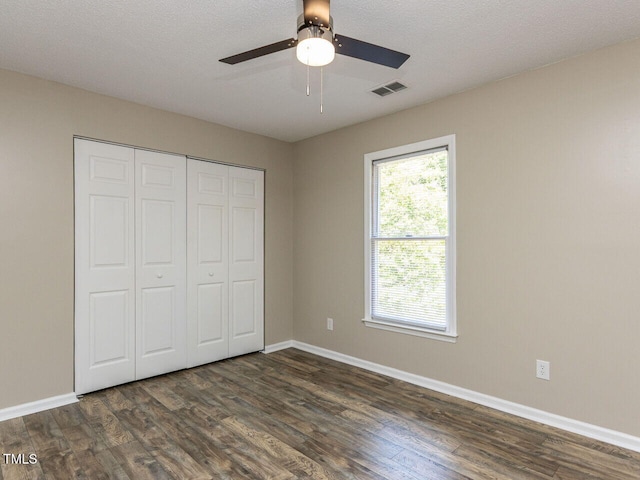 unfurnished bedroom featuring dark wood-style flooring, baseboards, a closet, and a ceiling fan