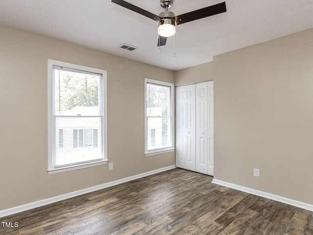 unfurnished bedroom with dark wood-style flooring, multiple windows, a closet, and baseboards