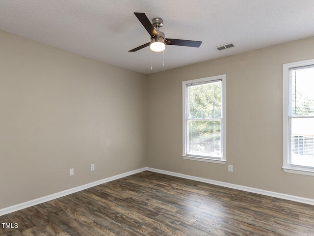 empty room featuring healthy amount of natural light, a ceiling fan, dark wood finished floors, and a textured ceiling